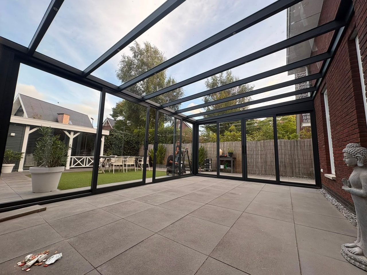 Blick aus einer Veranda mit Glasdach und umlaufenden Glasschiebewänden in den Garten