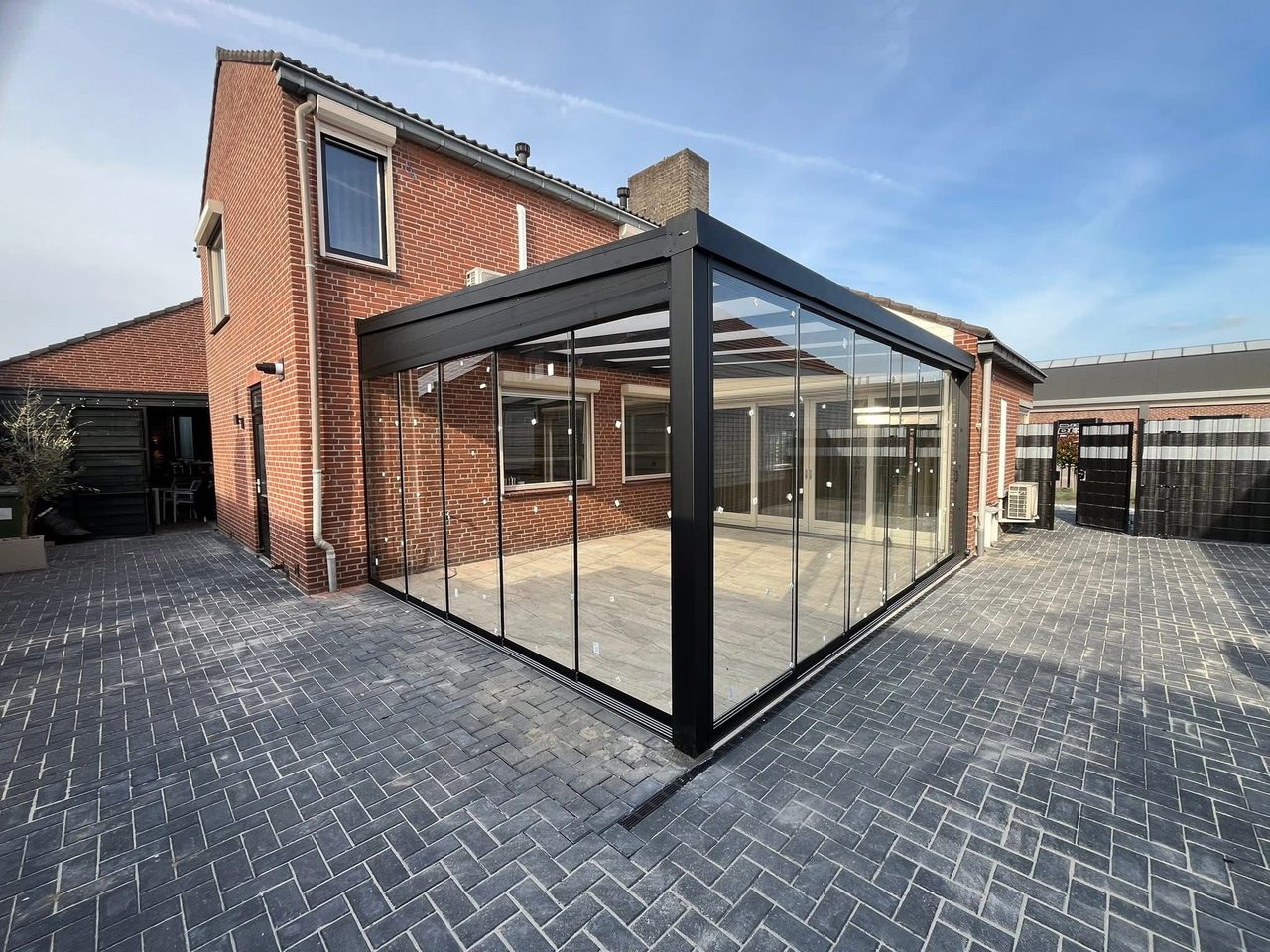 Eckansicht eines anthrazitfarbenen Sommergartens mit Glasschiebewänden an einem Backsteinhaus